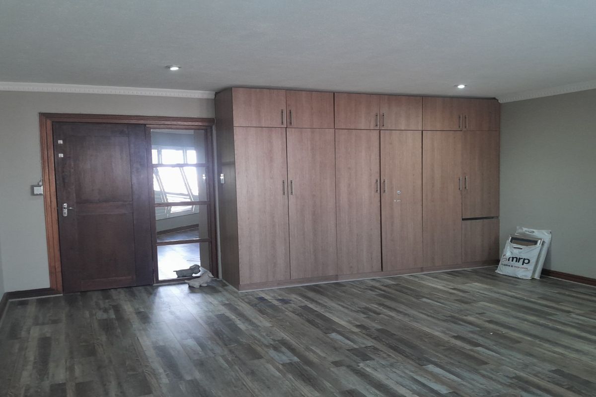 Spacious bedroom featuring extensive built-in wooden cabinetry, modern wood-look flooring, and a solid timber entrance door.
