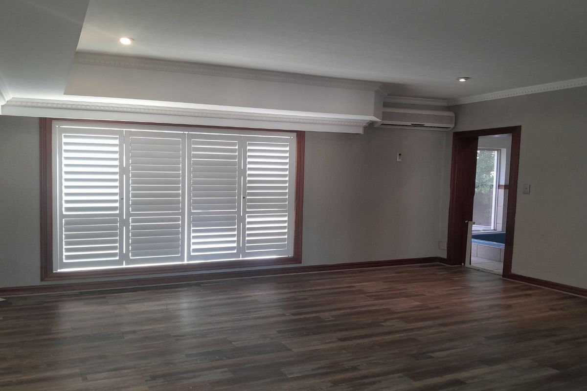 Spacious living area featuring wood-look flooring, recessed ceiling lighting, plantation shutters, and a wall-mounted air conditioning unit.