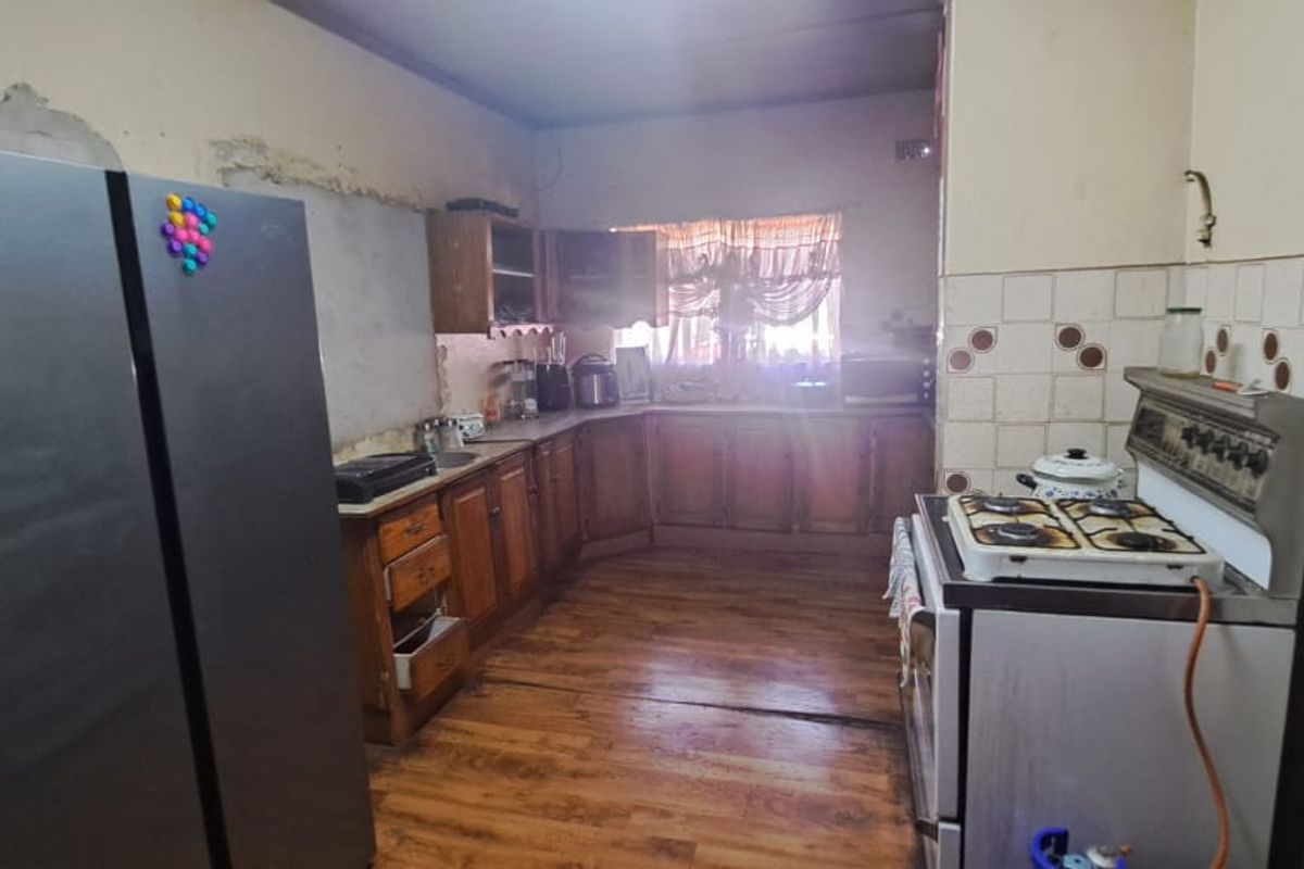 A dated kitchen featuring wooden cabinetry, tiled splashbacks, and a gas stove, requiring significant renovation and cosmetic updates to modernize the space.