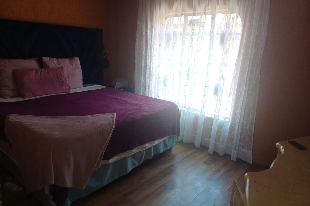 A bedroom featuring wood-look flooring and a window with sheer curtains, providing natural light to the space.