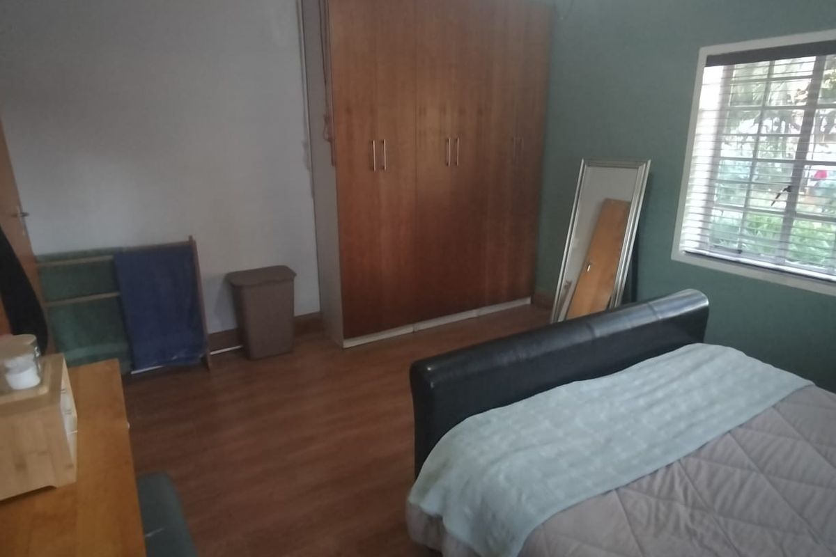 A bedroom featuring wood-look laminate flooring, a built-in wooden wardrobe, and a window with fitted blinds.