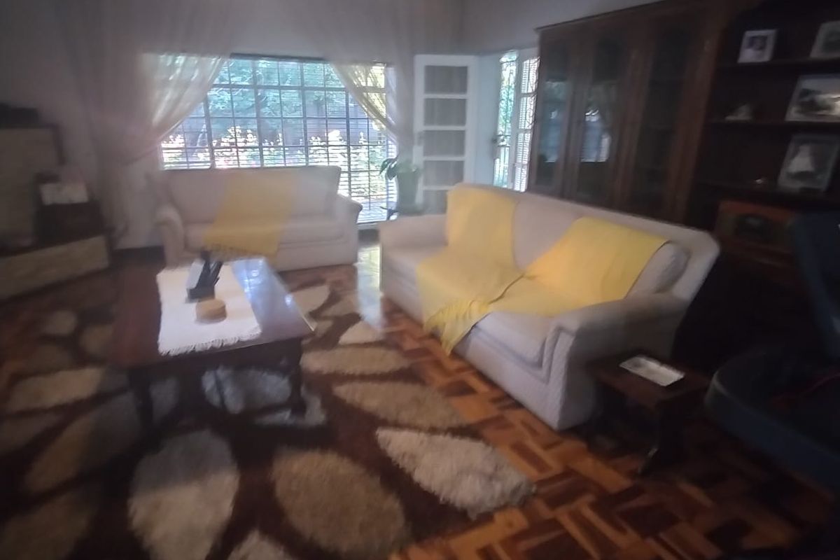 A spacious living room featuring classic parquet flooring, large windows providing natural light, and built-in wooden cabinetry.