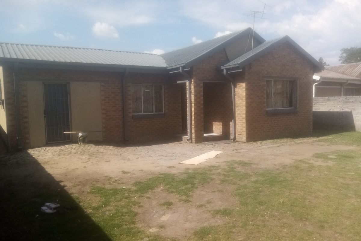 A single-story brick house with a metal roof, featuring a covered entrance and a spacious, partially landscaped yard.