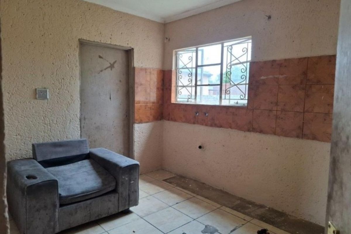 A basic utility or kitchen space featuring tiled flooring, wall-mounted splashback tiles, and security bars on the window.