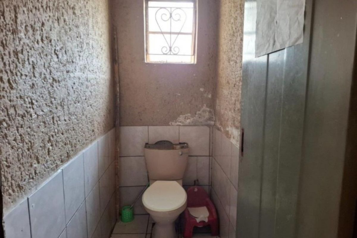 A small, dated bathroom featuring a standard toilet, tiled lower walls, and textured upper wall finishes requiring maintenance and cosmetic updates.