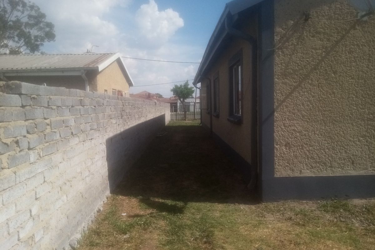 Side exterior view of the property featuring a textured facade, guttering system, and a long boundary wall separating the side yard area.