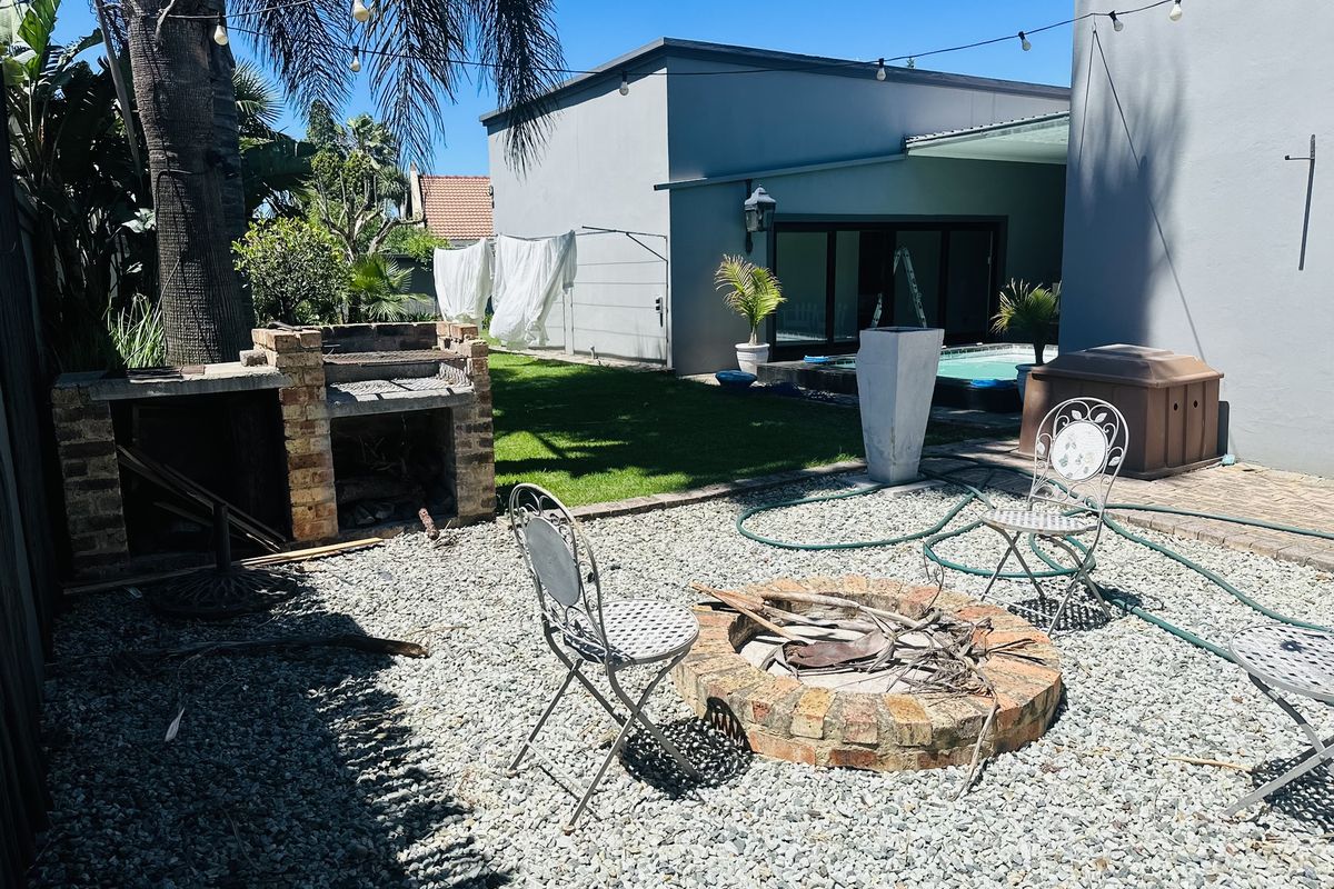 Outdoor entertainment area featuring a built-in brick braai, a circular fire pit, and a landscaped garden leading to a swimming pool.
