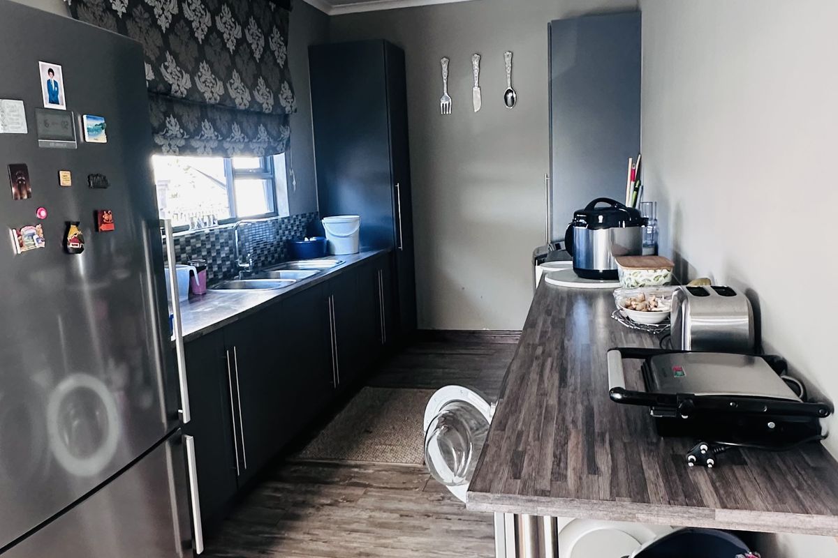 A functional galley-style kitchen featuring dark cabinetry, wood-look laminate flooring, a stainless steel sink, and a breakfast bar counter.