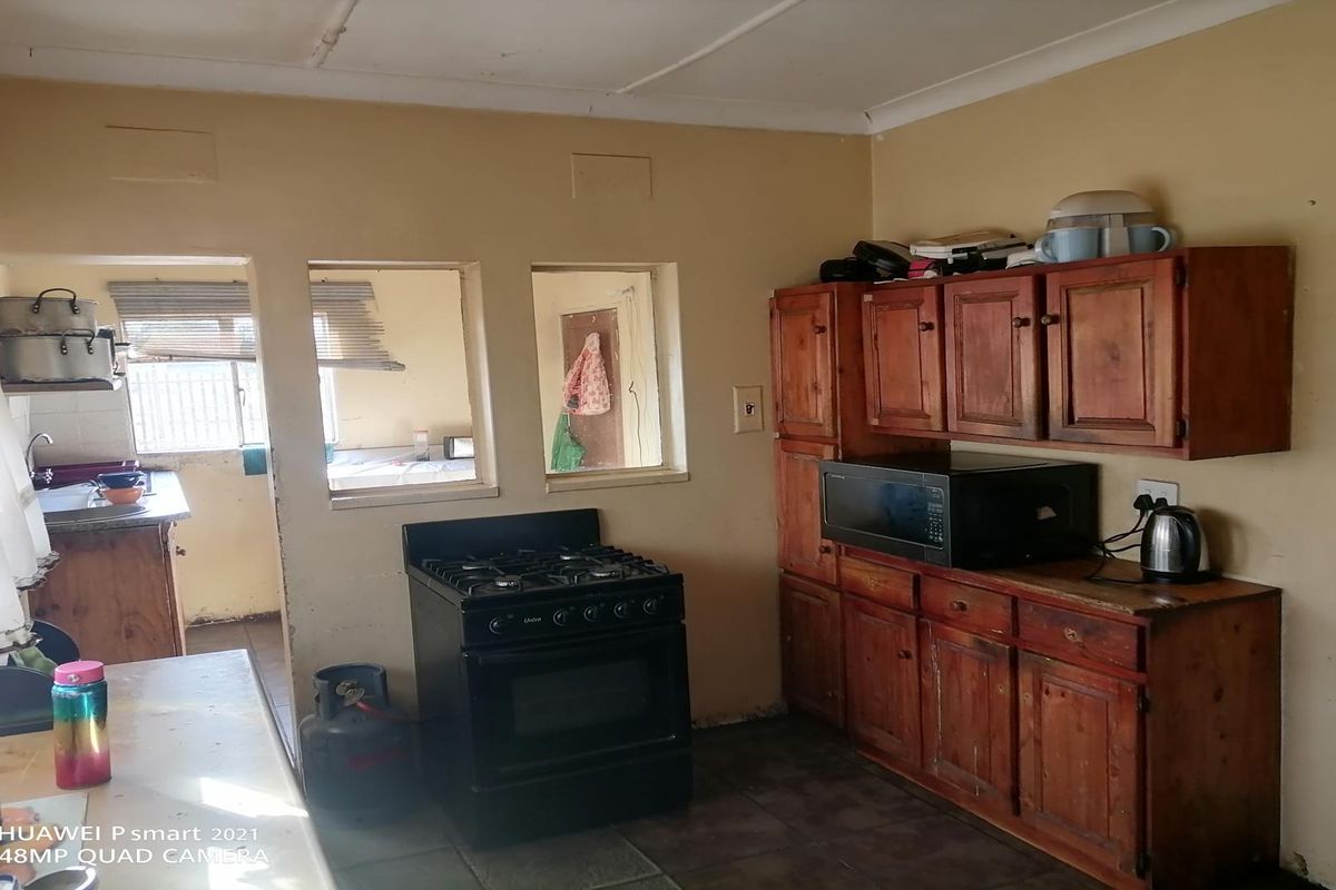 A functional kitchen featuring wooden cabinetry, a gas stove, and a serving window looking into an adjacent room.