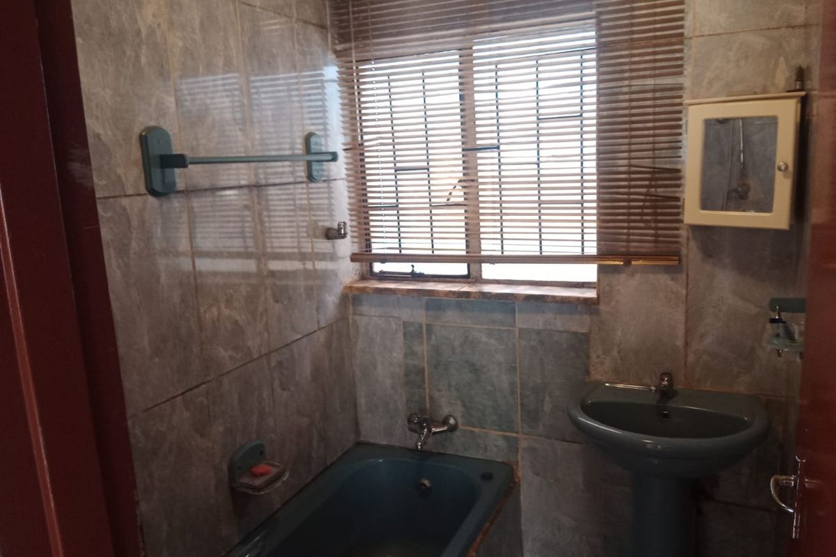 A dated bathroom featuring grey wall tiles, a matching grey pedestal basin, and a built-in bathtub with integrated plumbing fixtures.