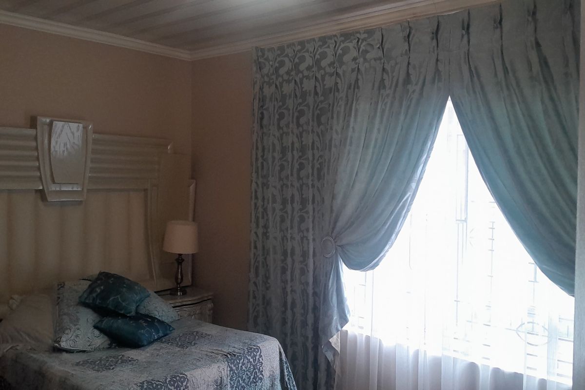 A bedroom featuring a built-in headboard and window with security bars, finished with neutral wall tones and decorative curtains.
