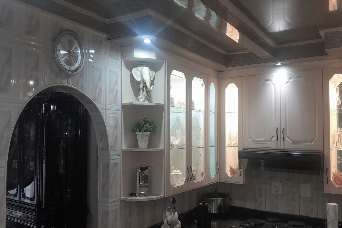 A kitchen featuring built-in cabinetry with glass-front display units, tiled walls, and an arched entryway leading to an adjacent room.