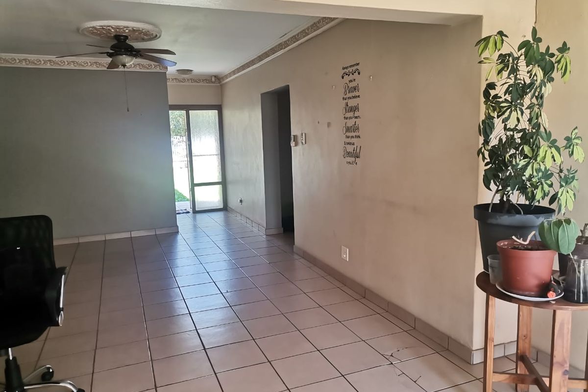 Spacious living area featuring tiled flooring, decorative ceiling rose with a fan, and direct access to the rear garden through a glass door.