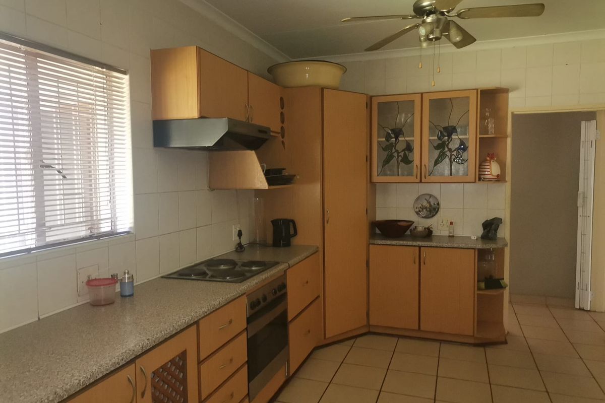 A functional kitchen featuring light wood cabinetry, a built-in oven and hob, extractor fan, tiled splashbacks, and ceramic floor tiles.