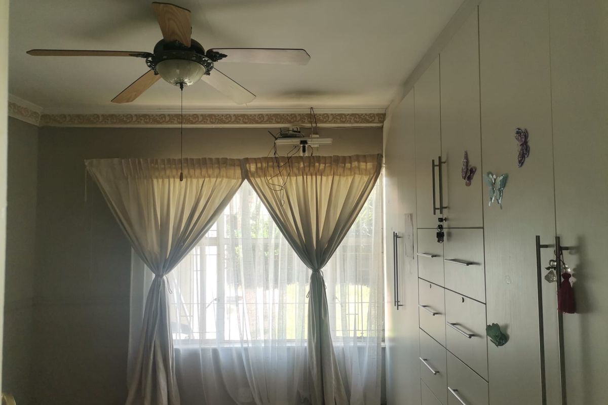 A bedroom featuring built-in floor-to-ceiling cabinetry, a ceiling fan, and window treatments with security bars.