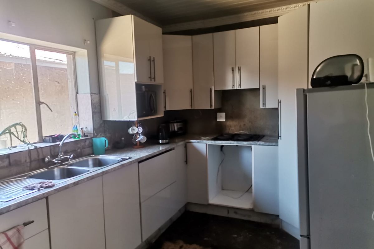 A compact kitchen featuring white cabinetry, a double-basin stainless steel sink, and a built-in hob, currently requiring floor and finish repairs.
