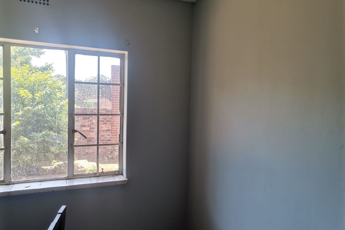 A simple bedroom featuring a large window with garden views, neutral walls, and a tiled windowsill.