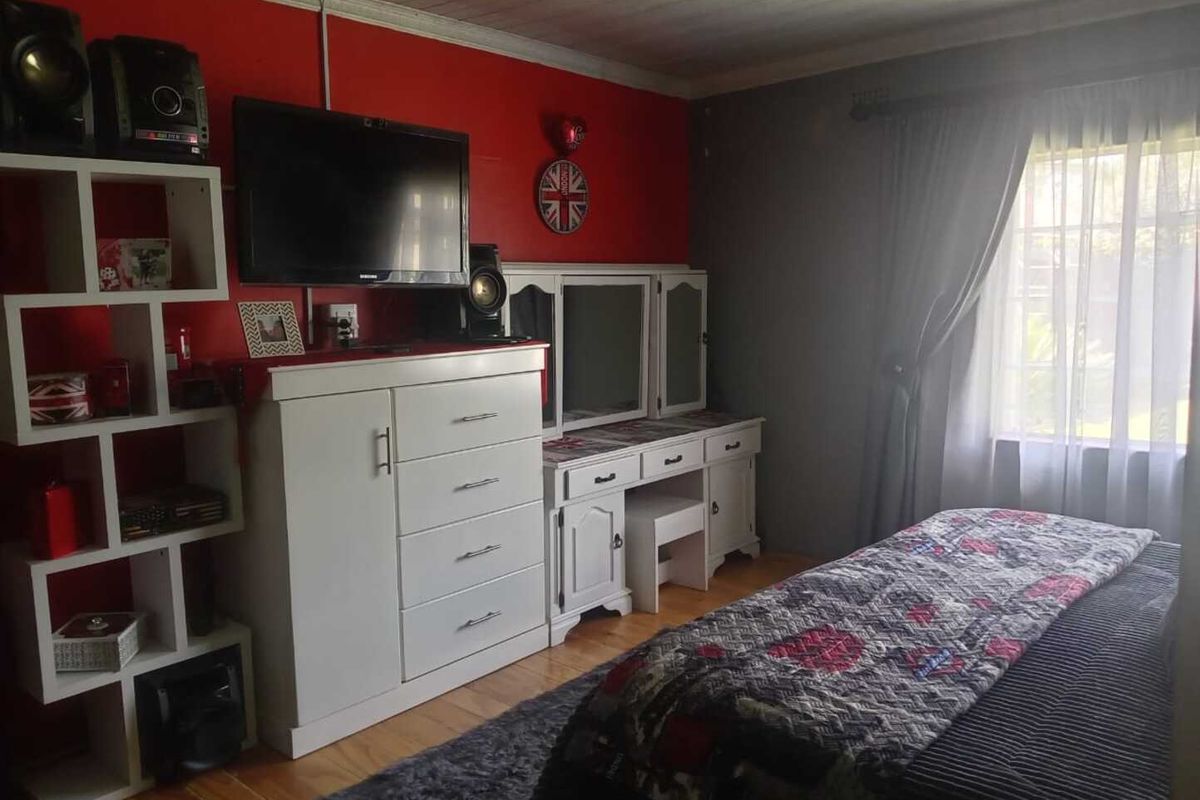 A bedroom featuring wooden flooring, a red accent wall, and a window with curtain treatments.