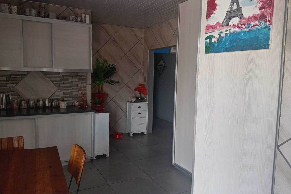 A functional kitchen area featuring built-in cabinetry, tiled splashbacks, and floor tiles, leading into an adjacent hallway space.