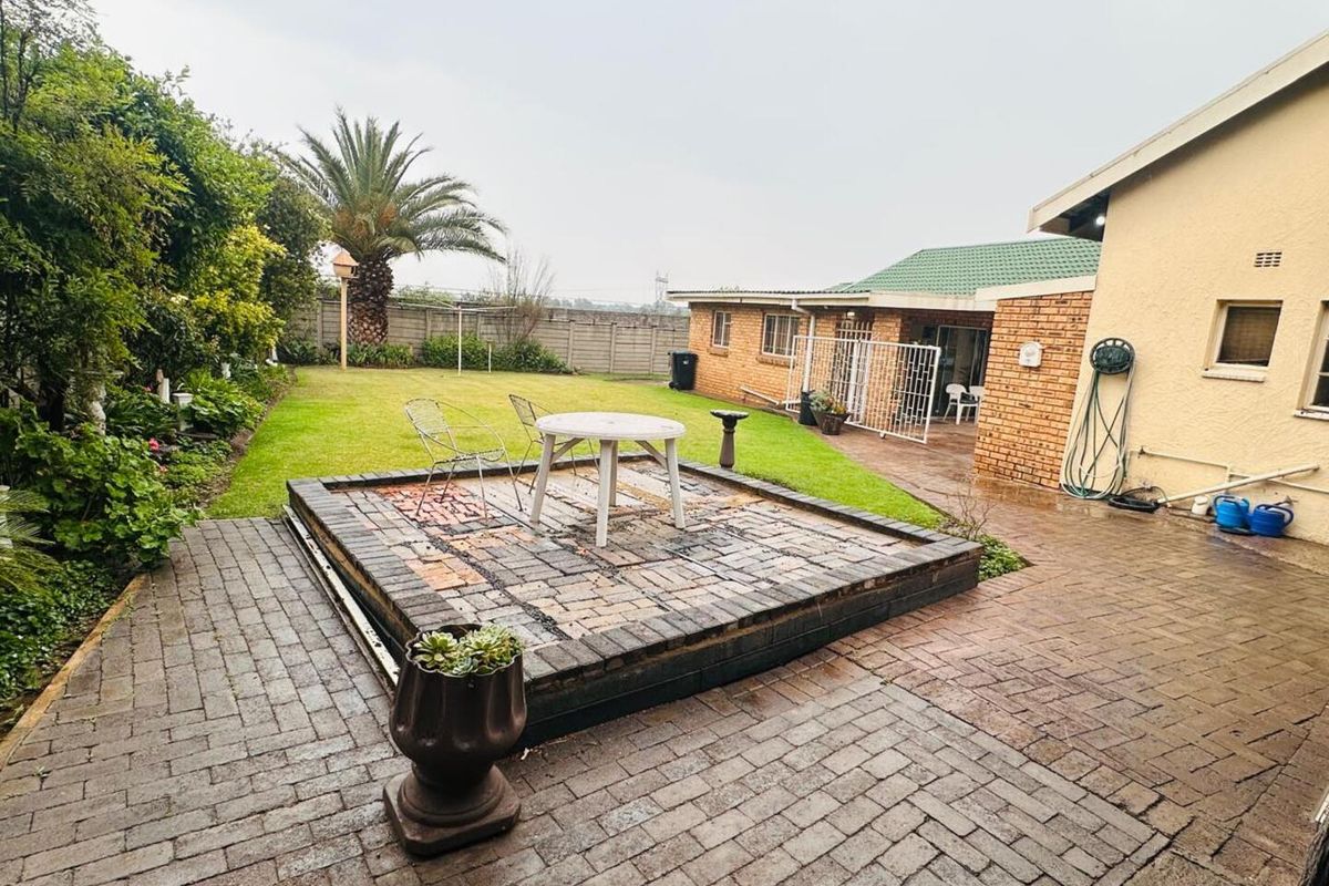 A spacious rear garden featuring a raised brick-paved patio area, established lawn, and perimeter boundary walls.