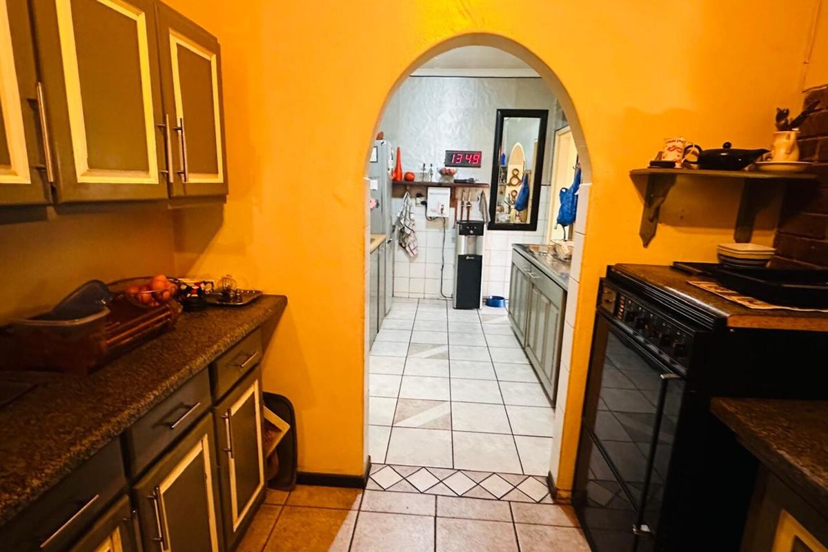 A functional kitchen featuring an arched doorway leading to a secondary prep area, with built-in cabinetry and tiled flooring throughout.