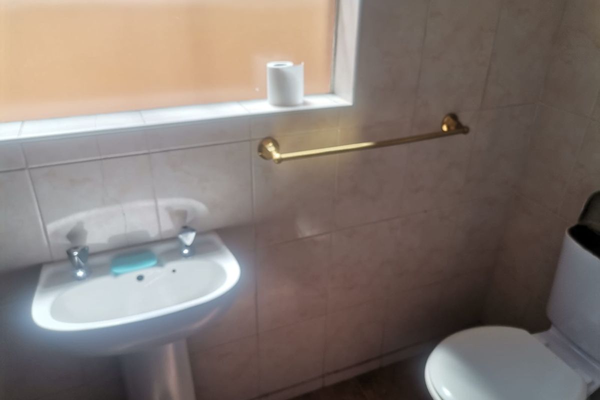 A functional bathroom featuring a pedestal basin, toilet, and wall-mounted towel rail with tiled walls and flooring.
