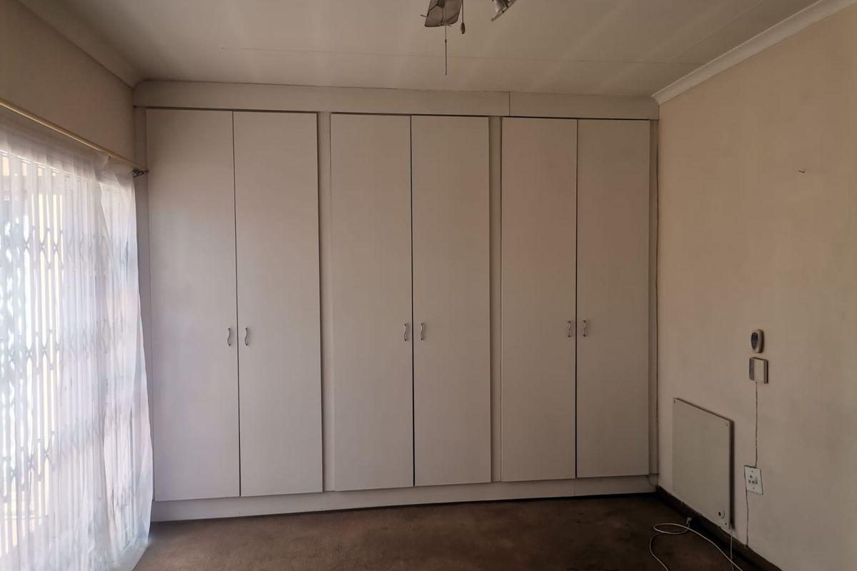 A bedroom featuring built-in cupboards, carpeted flooring, and a sliding door with security gate access.