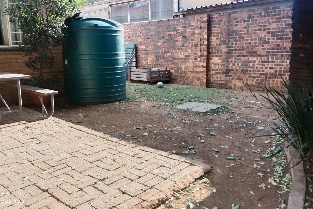 A rear garden area featuring a paved patio, a large water storage tank, and a brick boundary wall.