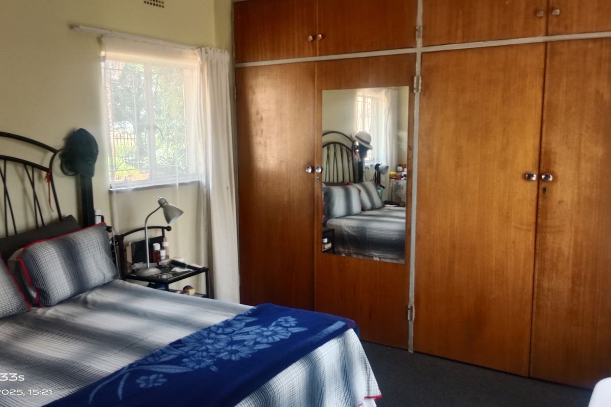A bedroom featuring large built-in wooden wardrobes with a central mirror and a window providing natural light.