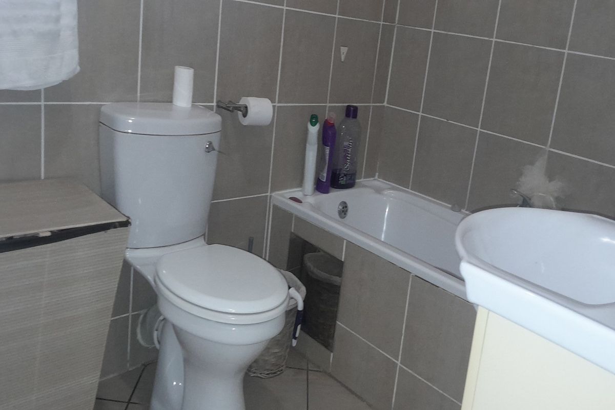 A functional bathroom featuring a standard toilet, a built-in bathtub with tiled surround, and a pedestal sink.