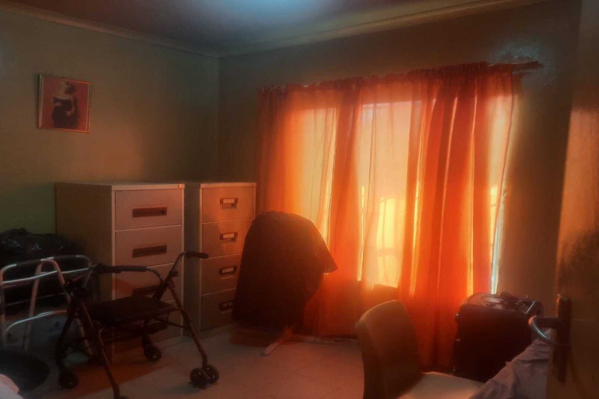 A bedroom featuring tiled flooring and natural light filtering through window curtains.