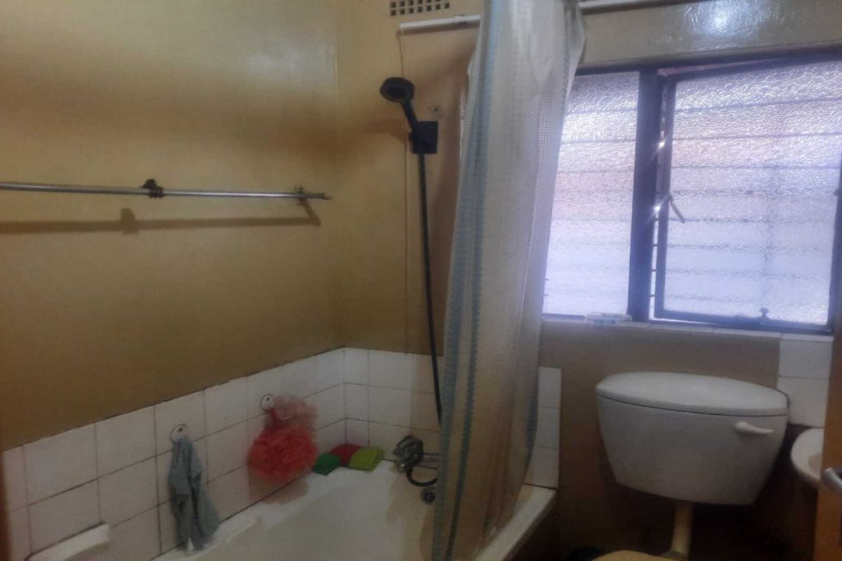 A functional bathroom featuring a bathtub with a shower attachment, a toilet, and a window with privacy glass.
