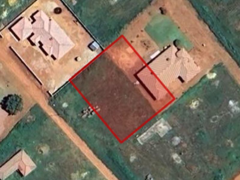 Aerial view of a vacant residential plot outlined in red, situated within an established neighborhood with surrounding residential properties.