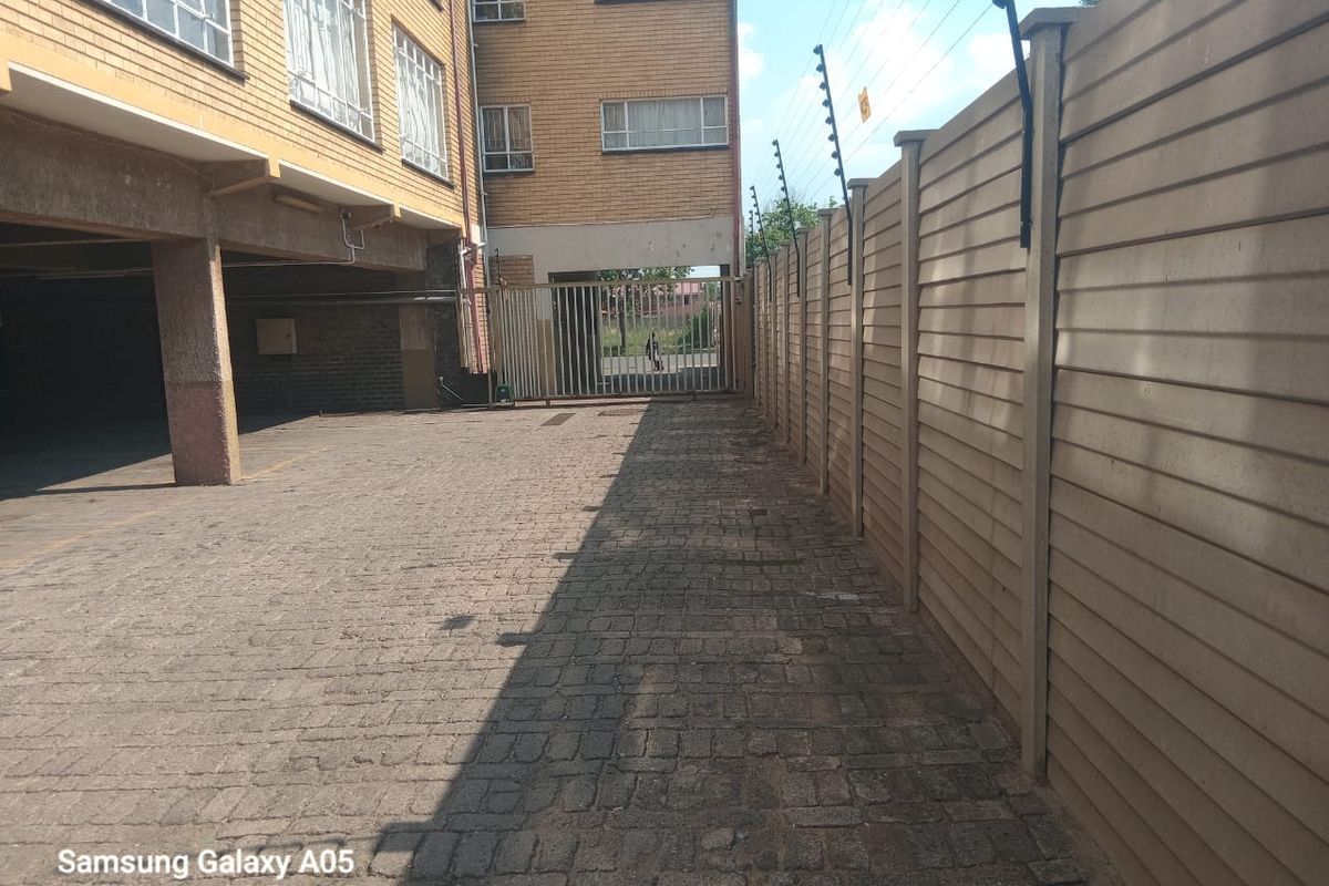 Exterior view of the apartment complex parking area featuring paved driveway, perimeter wall with electric fencing, and secure gated access.