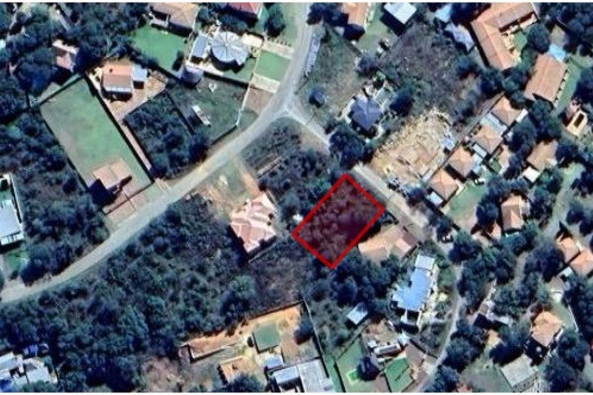 An aerial view of a vacant residential plot highlighted in red, situated within an established suburban neighborhood with surrounding vegetation and nearby housing.
