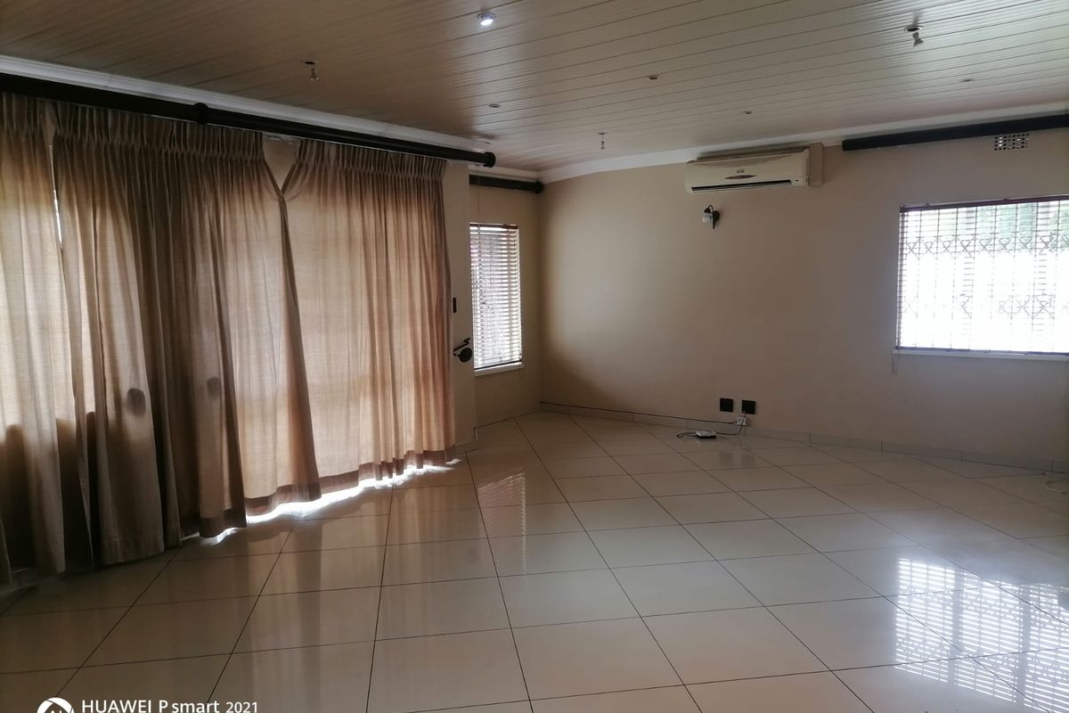 Spacious living area featuring tiled flooring, a wall-mounted air conditioning unit, and large windows with fitted curtains.