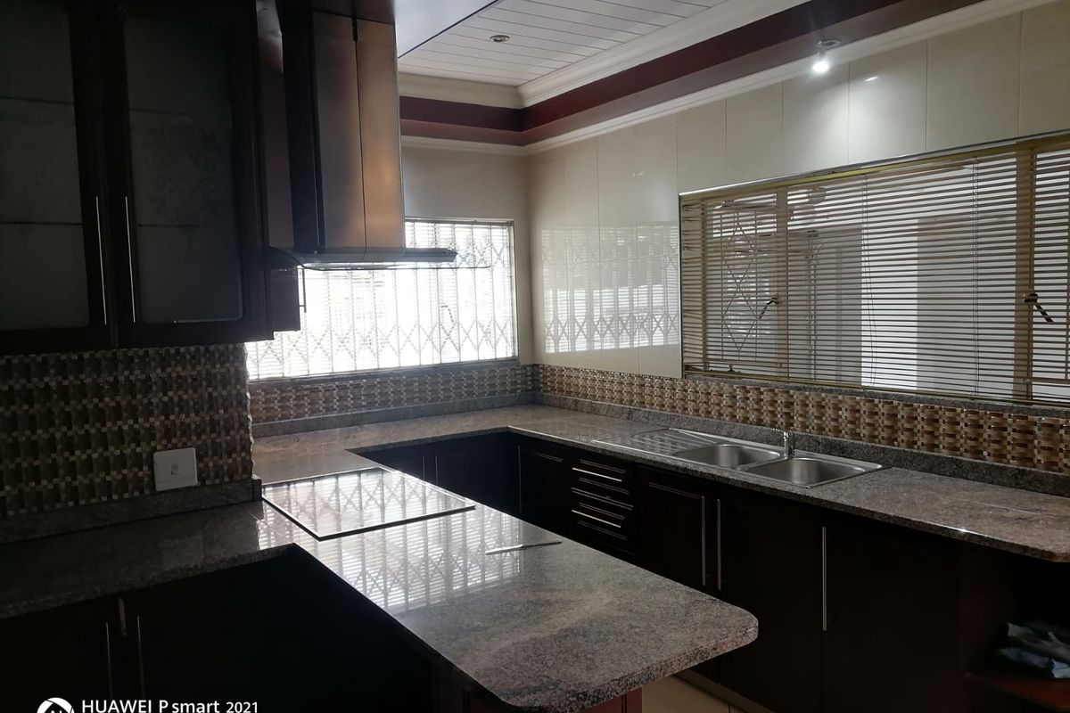 A functional kitchen featuring dark wood cabinetry, granite countertops, a stainless steel extractor fan, and a double-basin sink with tiled splashbacks.