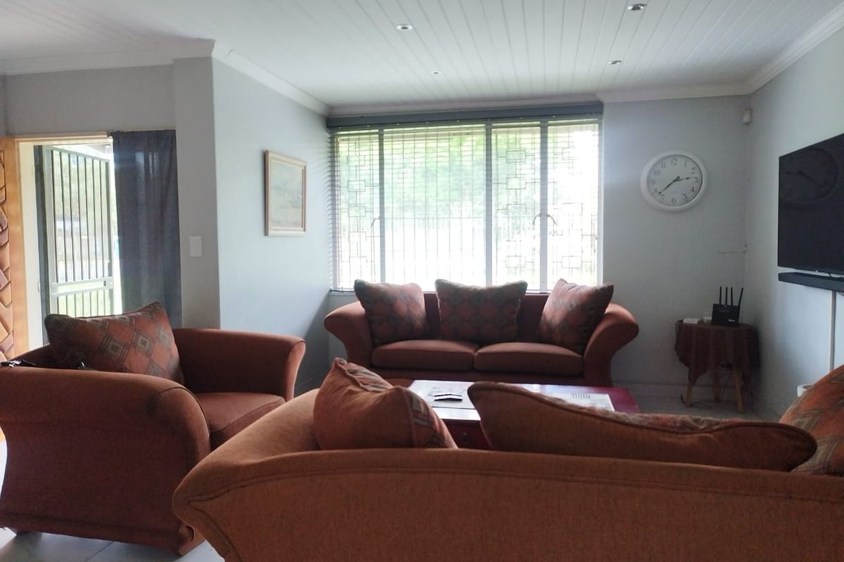 A comfortable living room featuring tiled flooring, recessed ceiling lighting, and large windows with security bars, providing natural light and access to the exterior.