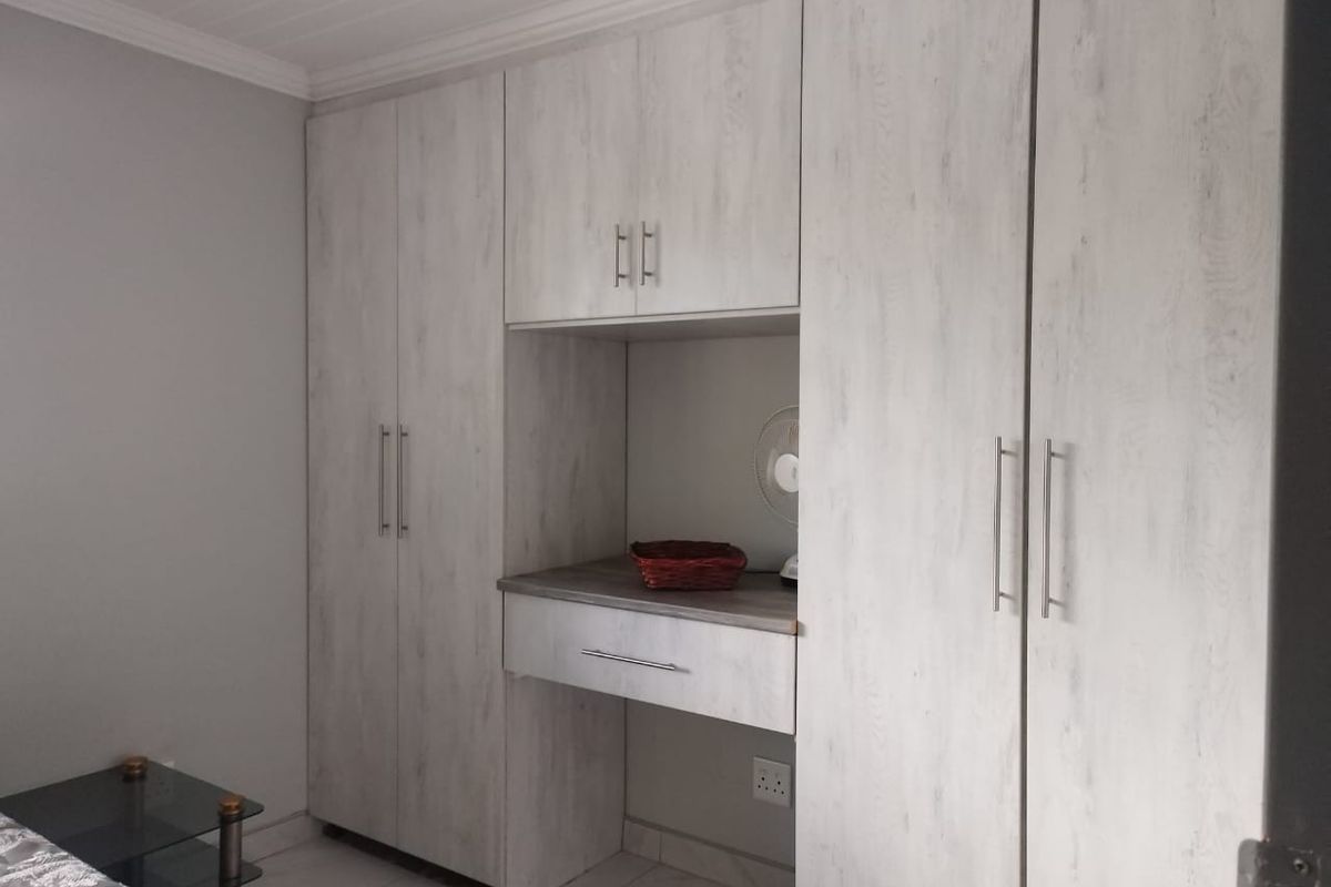 A bedroom featuring modern, light-toned built-in cupboards with integrated vanity or desk space and sleek metal handles.