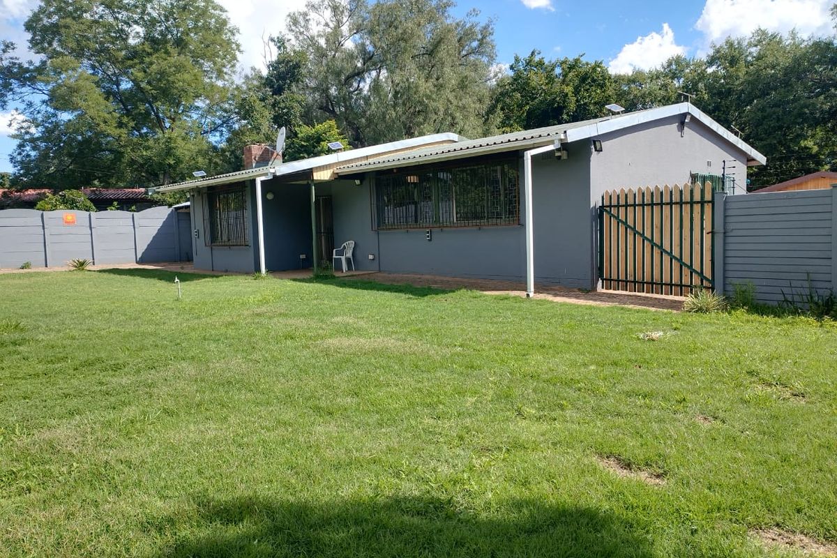 Rear view of the house featuring a spacious lawn, paved patio area, perimeter fencing, and security gates.