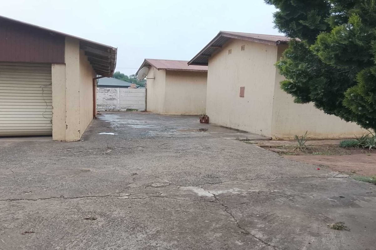 Exterior view of the property showing a concrete driveway, garage structure, and adjacent outbuildings with weathered finishes.