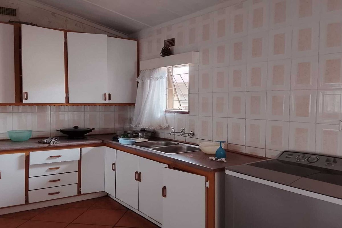 A dated kitchen featuring original white cabinetry, tiled splashbacks, and a double-basin sink, offering significant potential for a modern renovation.
