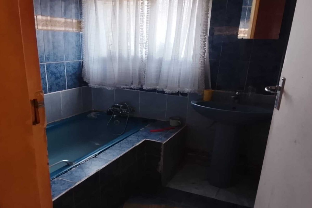 A dated bathroom featuring a built-in tiled bathtub and a pedestal sink with dark blue wall tiling.
