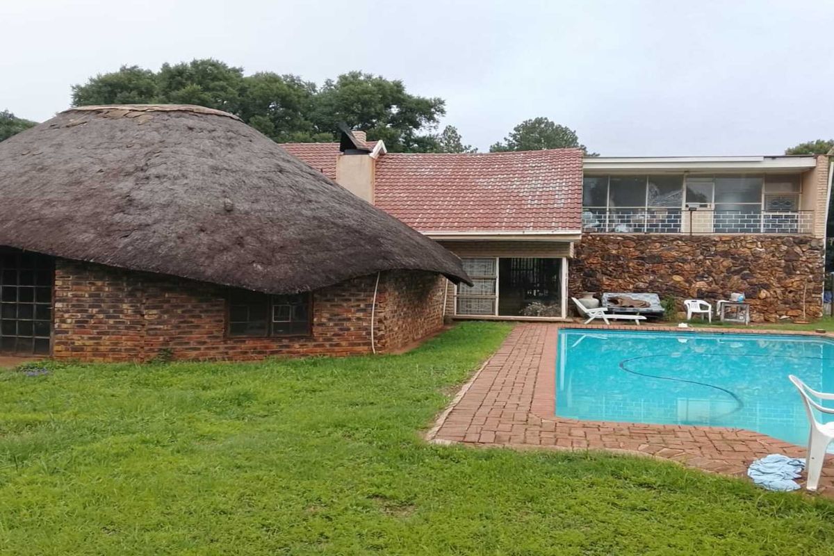 Rear exterior view featuring a swimming pool, brick patio, and a unique thatched roof structure alongside the main house.