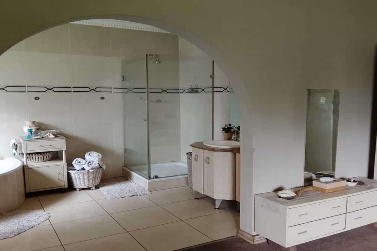 Spacious bathroom featuring a corner bathtub, a glass-enclosed shower, and a built-in vanity unit with a basin, separated by a decorative archway.