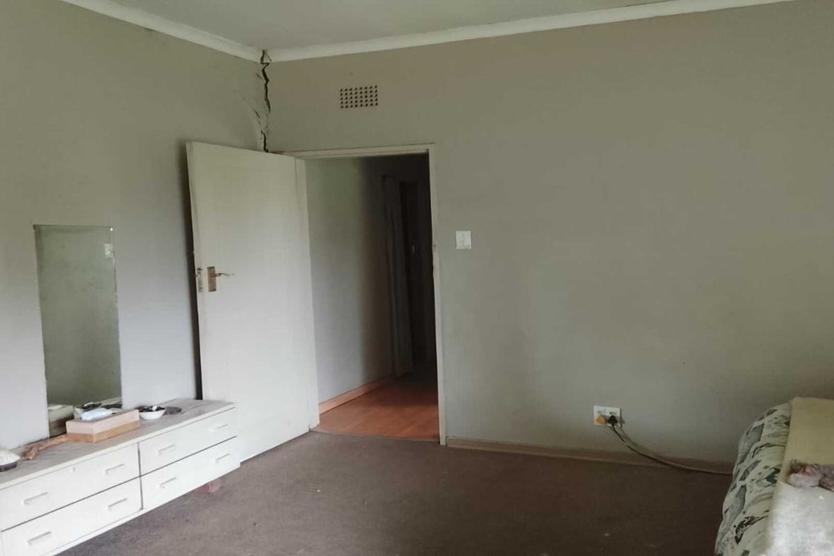 A bedroom featuring carpeted flooring and a prominent structural crack in the wall above the doorway.