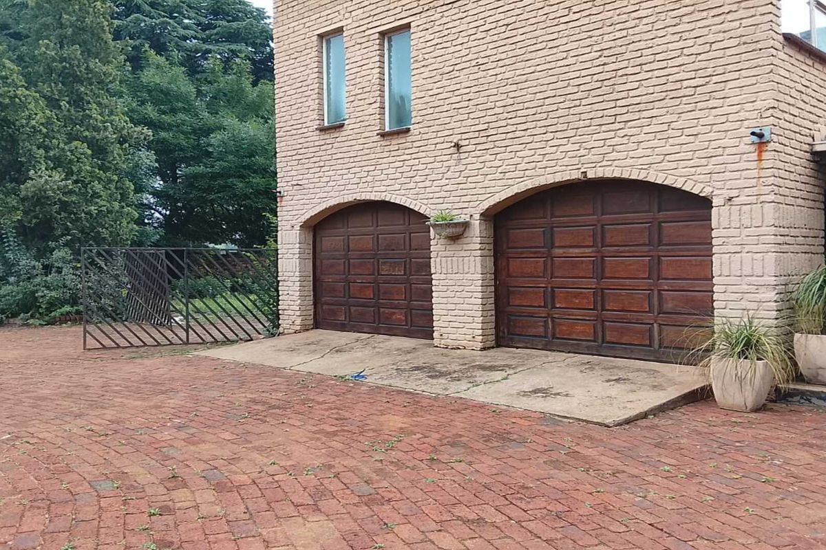 A double garage with arched wooden doors and brick facade, featuring a paved driveway and surrounding garden area.