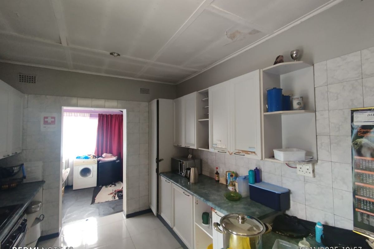 A functional kitchen featuring white cabinetry, tiled walls, and laminate countertops, with an adjacent utility area visible through the doorway.