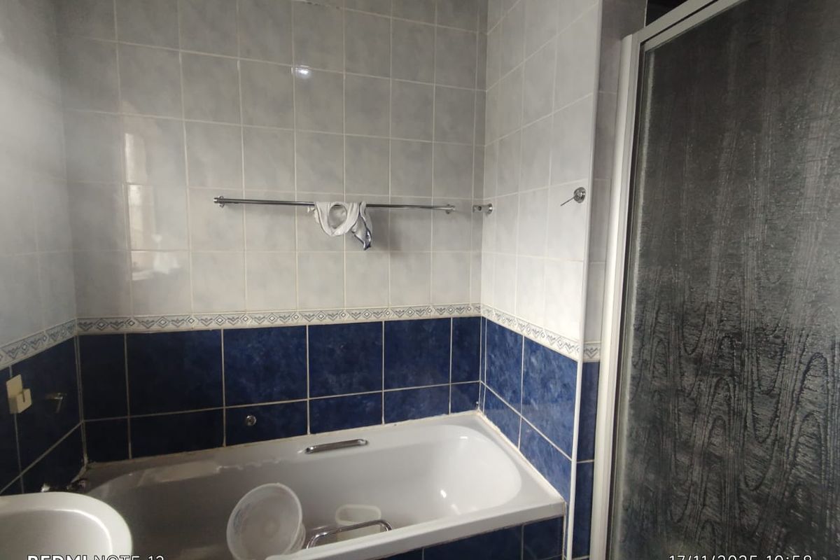A dated bathroom featuring a built-in bathtub with blue and white wall tiling and a separate shower enclosure.