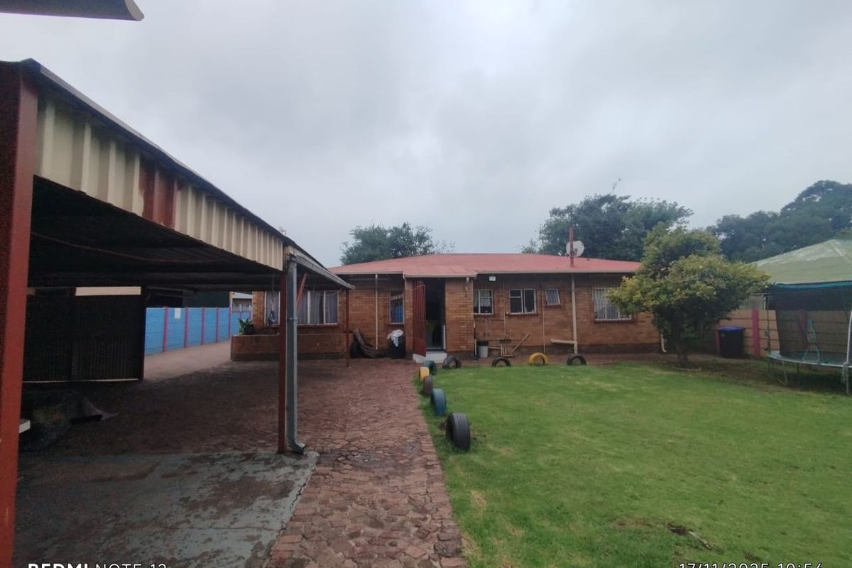 Rear view of the property featuring a brick facade, a covered carport area, and a spacious garden with established lawn.